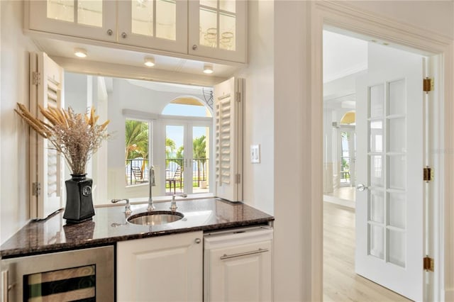 bar with dark stone countertops, white cabinetry, light hardwood / wood-style floors, and sink