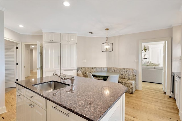 kitchen featuring a kitchen island with sink, pendant lighting, sink, light hardwood / wood-style floors, and white cabinetry