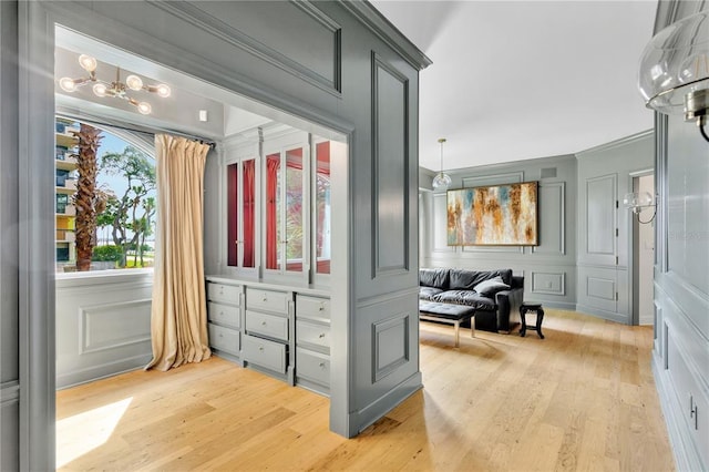 doorway with crown molding, light wood-type flooring, and an inviting chandelier