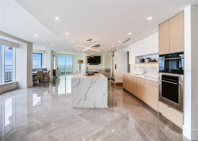 kitchen with sink, light stone countertops, a kitchen island, light brown cabinetry, and stainless steel double oven