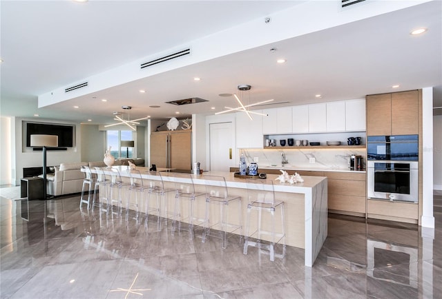 kitchen featuring white cabinetry, sink, double oven, and a breakfast bar