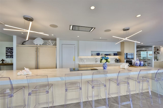 kitchen with white cabinets, backsplash, a kitchen bar, paneled built in refrigerator, and light stone counters