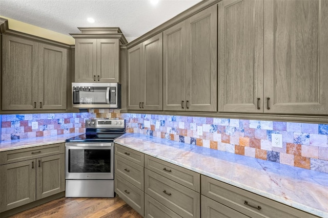 kitchen with a textured ceiling, appliances with stainless steel finishes, dark hardwood / wood-style floors, and backsplash