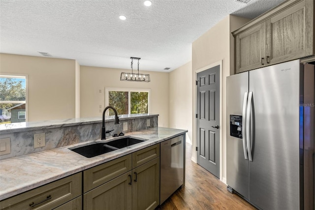 kitchen with stainless steel appliances, sink, light stone countertops, light hardwood / wood-style flooring, and decorative light fixtures