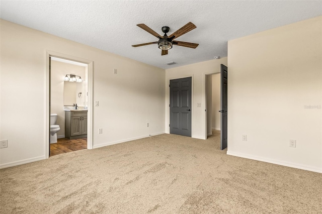 unfurnished bedroom featuring ensuite bathroom, ceiling fan, a textured ceiling, and light colored carpet