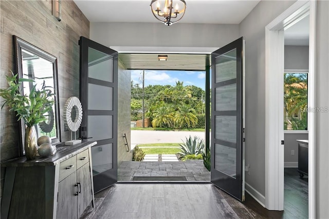 entryway featuring an inviting chandelier, a wealth of natural light, dark wood-type flooring, and wood walls