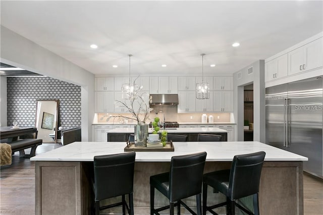 kitchen featuring white cabinetry, a spacious island, stainless steel built in refrigerator, and hanging light fixtures