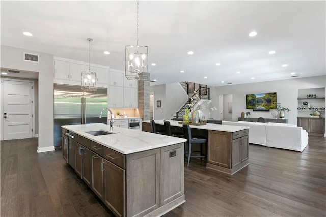 kitchen featuring sink, a center island with sink, stainless steel built in fridge, white cabinets, and hanging light fixtures