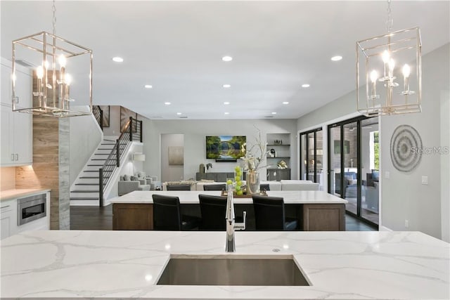 kitchen with hanging light fixtures, light stone countertops, stainless steel microwave, and an island with sink