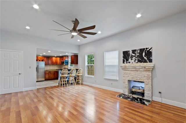 living room with ceiling fan, a stone fireplace, and light wood-type flooring