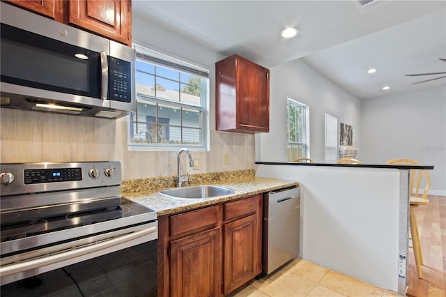 kitchen featuring sink, appliances with stainless steel finishes, tasteful backsplash, light stone countertops, and kitchen peninsula