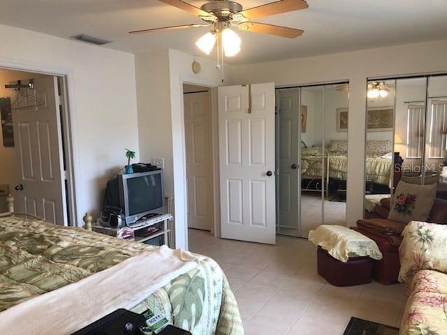 bedroom featuring light tile flooring, ceiling fan, and multiple closets