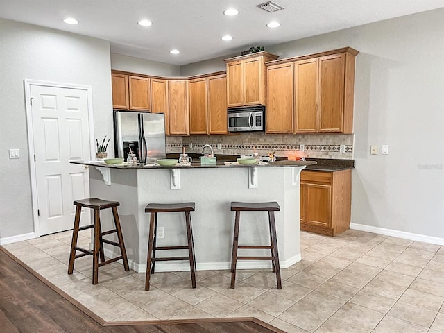 kitchen with appliances with stainless steel finishes, an island with sink, backsplash, and light wood-type flooring