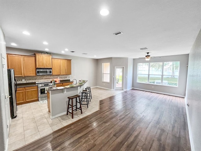 kitchen with light hardwood / wood-style floors, stainless steel appliances, ceiling fan, a breakfast bar, and backsplash