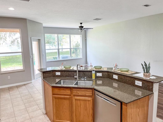 kitchen with sink, dark stone countertops, dishwasher, a center island with sink, and a wealth of natural light