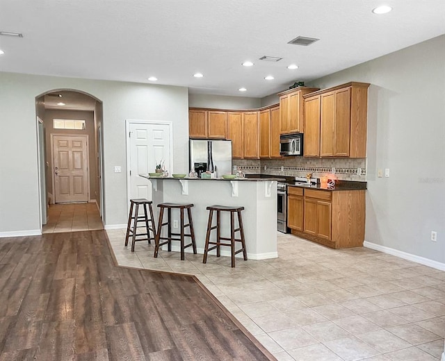 kitchen with an island with sink, stainless steel appliances, a kitchen breakfast bar, light hardwood / wood-style flooring, and backsplash