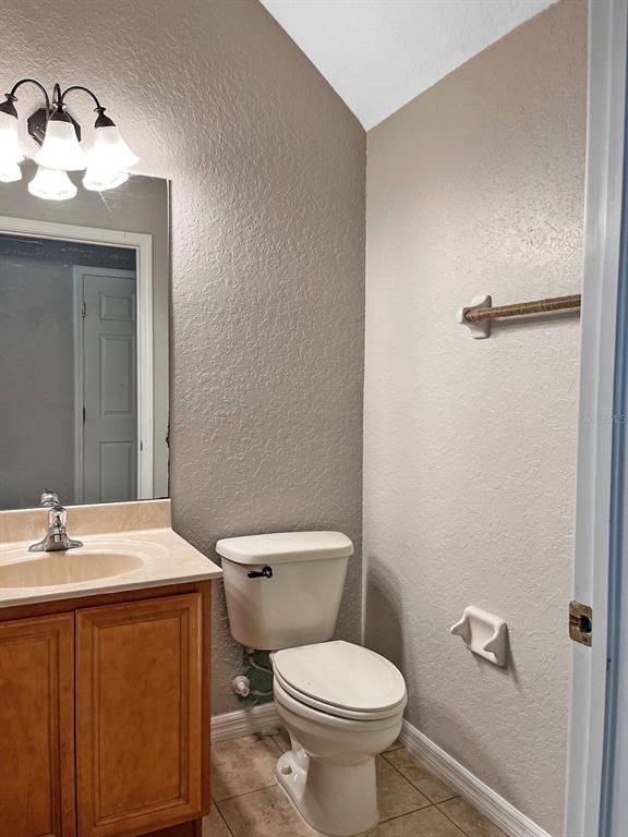 bathroom featuring tile floors, toilet, vanity, and lofted ceiling