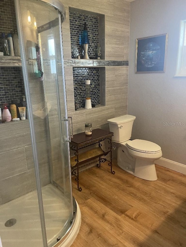 bathroom with a shower with shower door, hardwood / wood-style floors, tile walls, and toilet