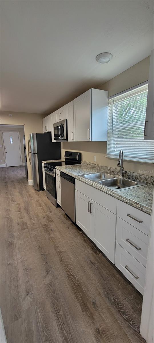 kitchen with sink, hardwood / wood-style flooring, light stone counters, white cabinetry, and stainless steel appliances