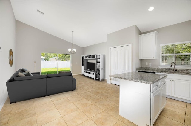 kitchen with sink, vaulted ceiling, a kitchen island, light stone counters, and white cabinetry