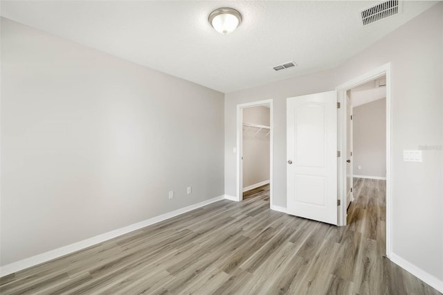 unfurnished bedroom with a textured ceiling, light hardwood / wood-style floors, a spacious closet, and a closet