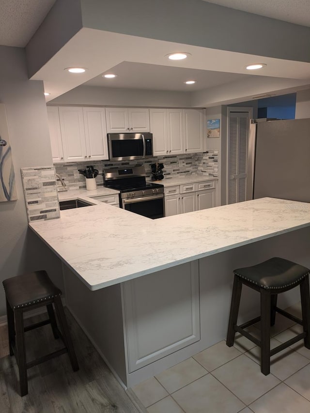 kitchen with white cabinets, backsplash, kitchen peninsula, a breakfast bar area, and stainless steel appliances