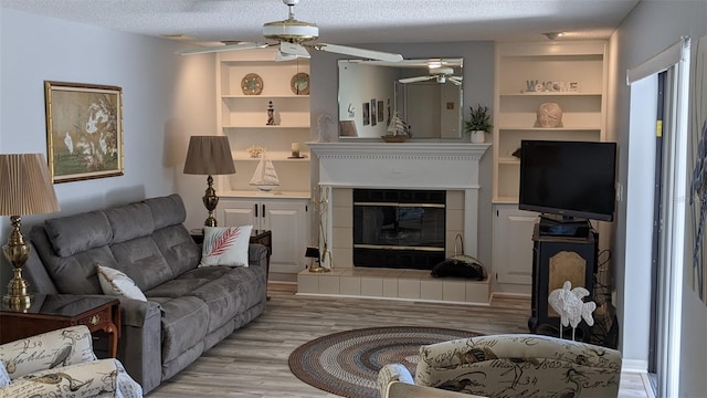 living room featuring a textured ceiling, a fireplace, ceiling fan, and light hardwood / wood-style flooring