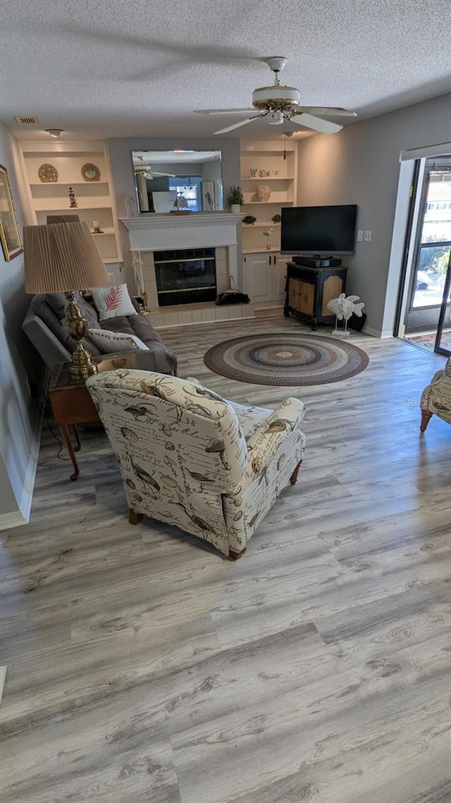 living room with a textured ceiling, a tile fireplace, ceiling fan, and light hardwood / wood-style flooring