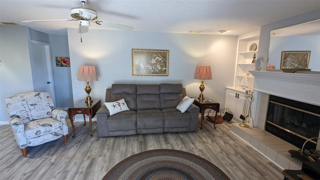 living room with ceiling fan, a textured ceiling, light hardwood / wood-style flooring, and a tile fireplace