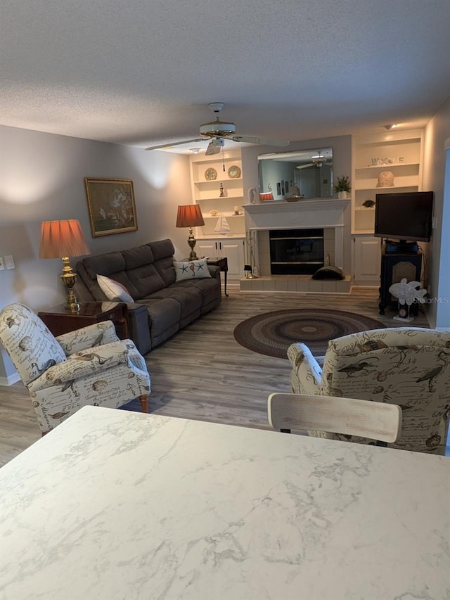 living room featuring ceiling fan, a textured ceiling, a tiled fireplace, and wood-type flooring