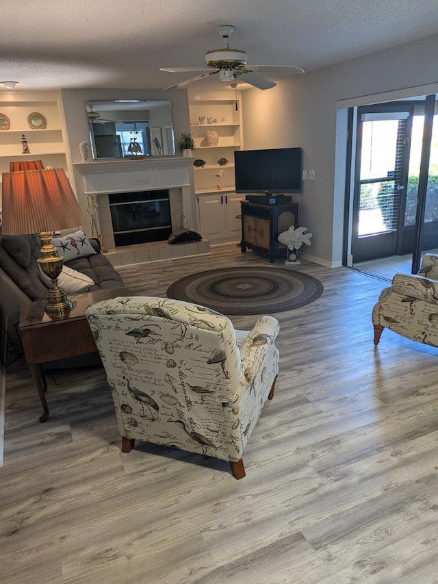 living room featuring ceiling fan, built in features, a textured ceiling, light hardwood / wood-style flooring, and a tile fireplace