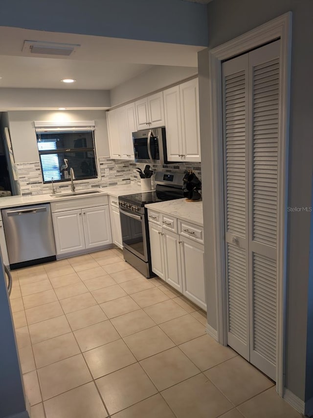 kitchen featuring sink, white cabinets, stainless steel appliances, backsplash, and light tile patterned floors