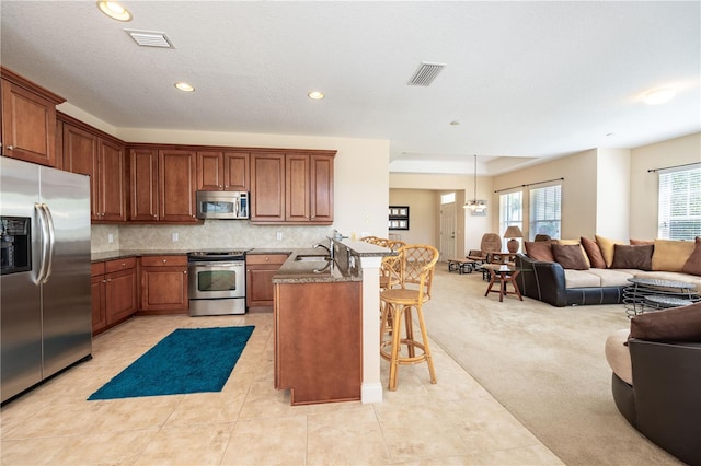 kitchen featuring a kitchen breakfast bar, tasteful backsplash, light colored carpet, hanging light fixtures, and appliances with stainless steel finishes