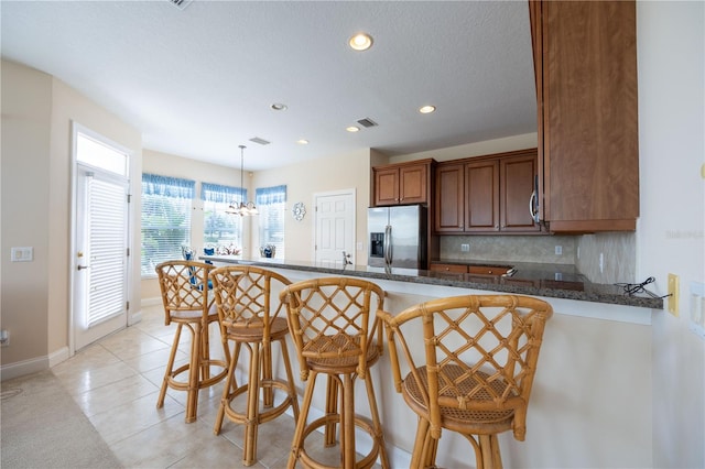 kitchen with a breakfast bar area, stainless steel refrigerator with ice dispenser, backsplash, and kitchen peninsula