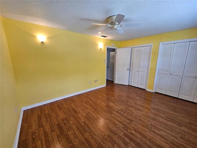 unfurnished bedroom with dark hardwood / wood-style floors, two closets, a textured ceiling, and ceiling fan