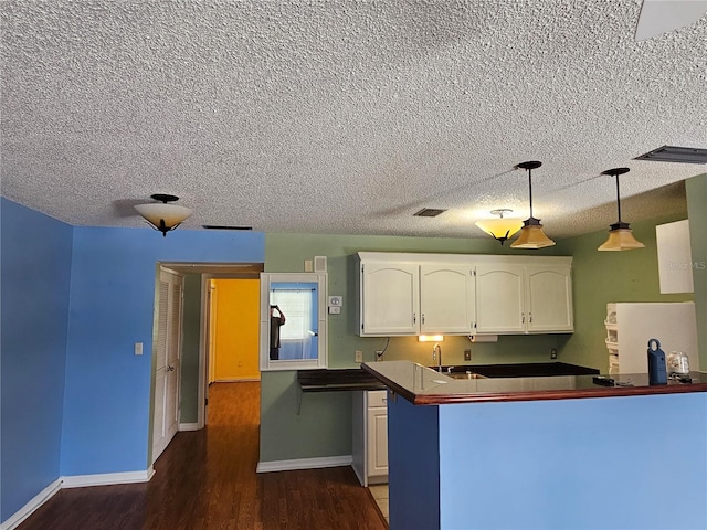 kitchen featuring decorative light fixtures, a textured ceiling, white cabinets, and dark wood-type flooring