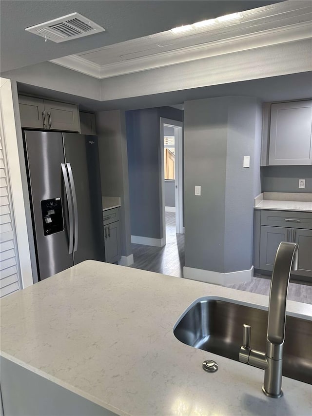 kitchen featuring wood-type flooring, ornamental molding, gray cabinetry, stainless steel refrigerator with ice dispenser, and sink