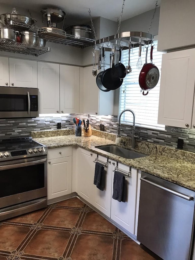 kitchen featuring sink, dark tile flooring, appliances with stainless steel finishes, backsplash, and white cabinetry