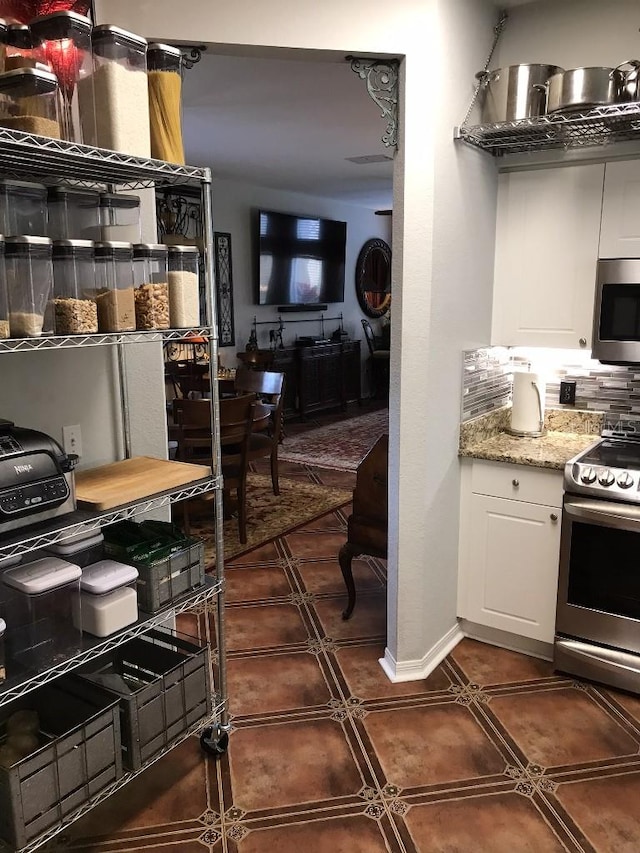 interior space with dark tile flooring, appliances with stainless steel finishes, light stone countertops, tasteful backsplash, and white cabinetry