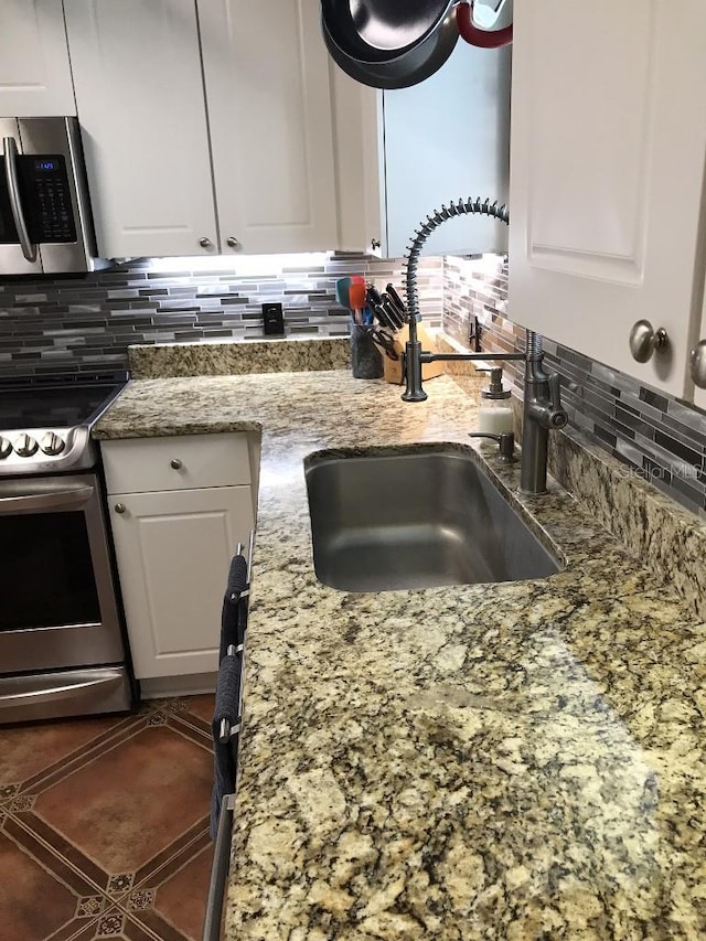 kitchen featuring appliances with stainless steel finishes, white cabinetry, dark stone counters, and tasteful backsplash