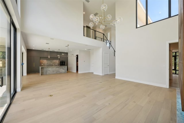 unfurnished living room featuring light wood-type flooring, a towering ceiling, and a notable chandelier