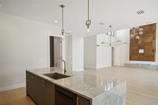 kitchen with pendant lighting, a large island with sink, sink, black dishwasher, and light stone counters