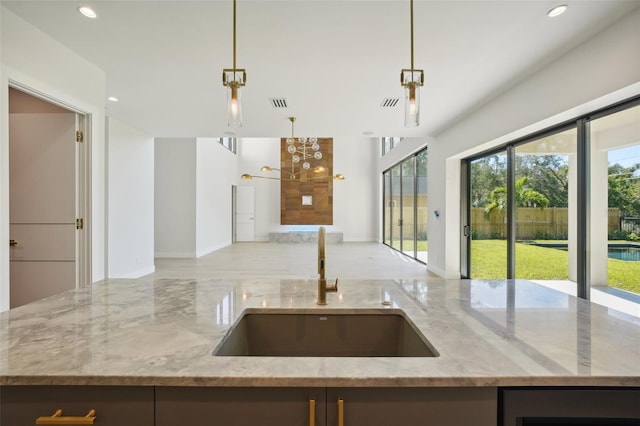 kitchen featuring light stone counters, sink, a kitchen island with sink, and decorative light fixtures