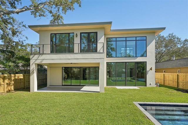 back of property featuring a balcony, a patio area, and a lawn