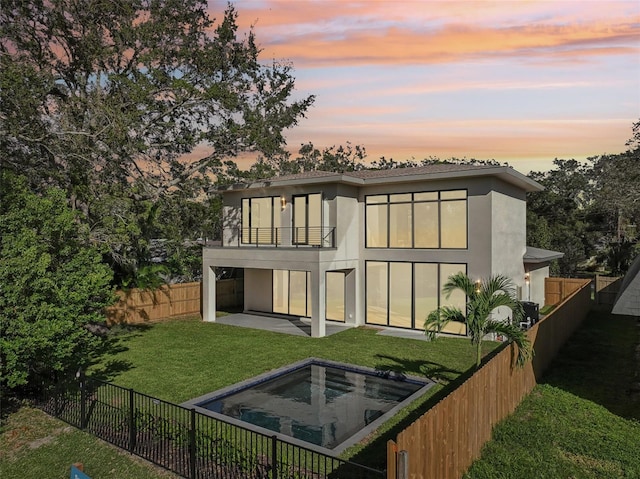 back house at dusk featuring a patio area, a balcony, and a yard