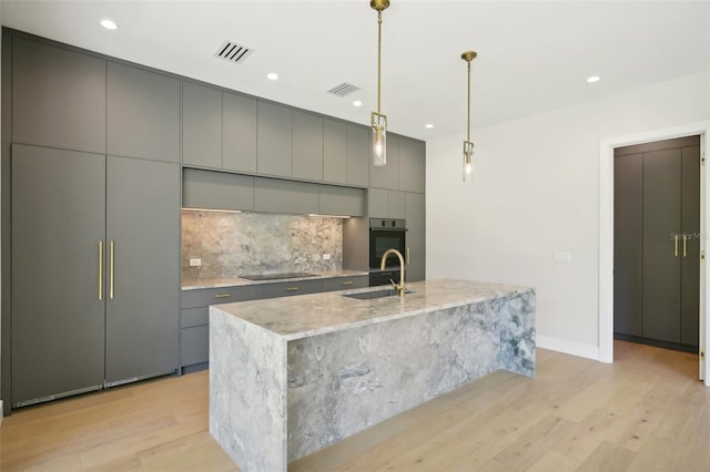 kitchen with hanging light fixtures, gray cabinets, sink, and a large island with sink