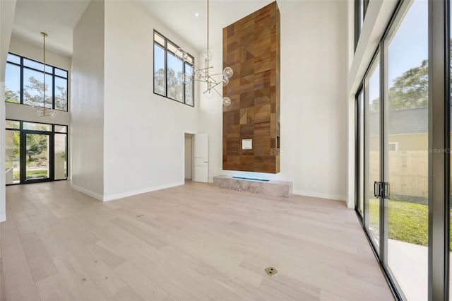 unfurnished living room with a towering ceiling, light hardwood / wood-style flooring, and an inviting chandelier