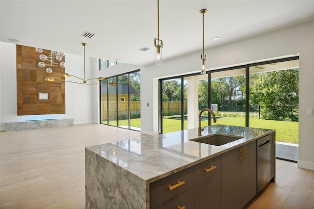 kitchen featuring dishwasher, a center island with sink, sink, hanging light fixtures, and light stone counters