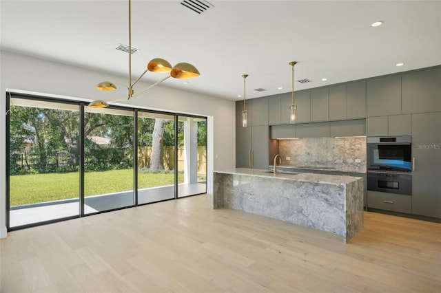 kitchen with light stone countertops, light hardwood / wood-style floors, gray cabinetry, and sink