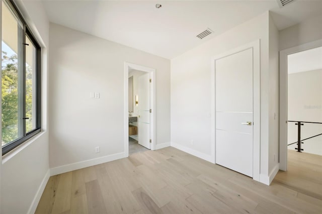 unfurnished bedroom with ensuite bathroom and light hardwood / wood-style flooring